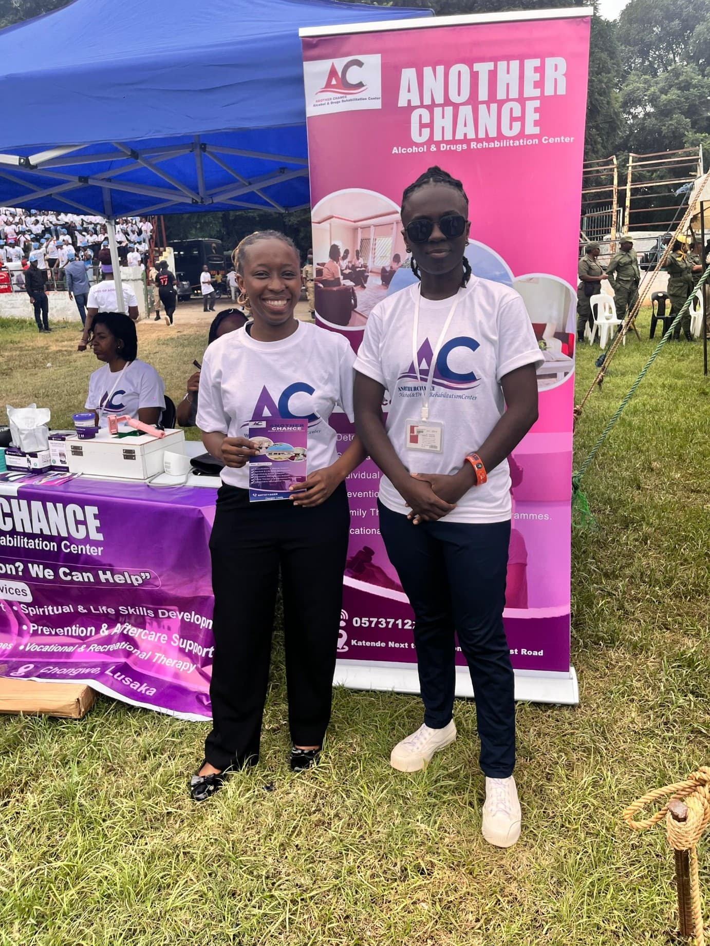 Two Another Chance team members standing beside a rehabilitation center banner at a public event